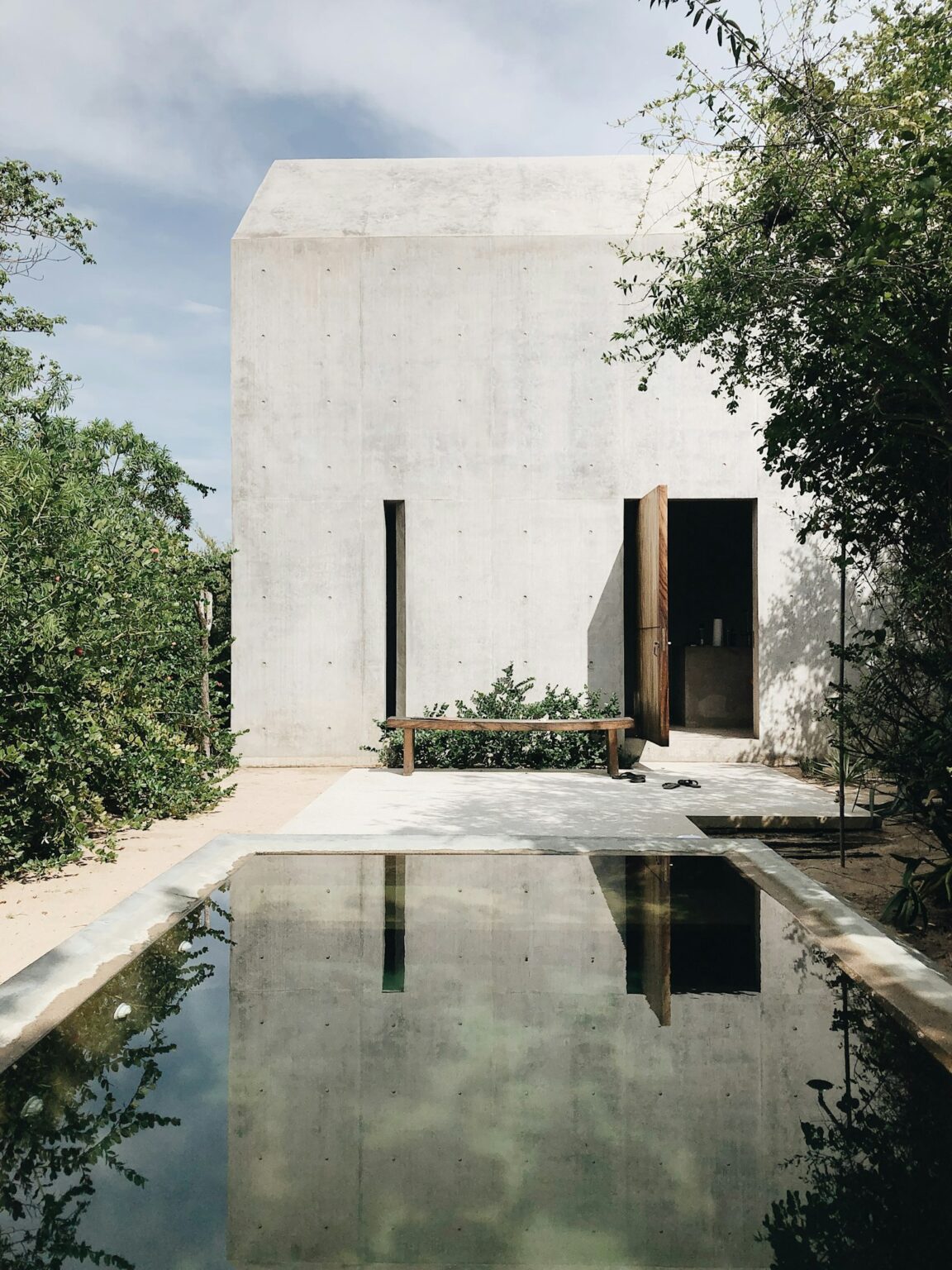 Casa de hormigón visto reflejada en un estanque rodeado de vegetación