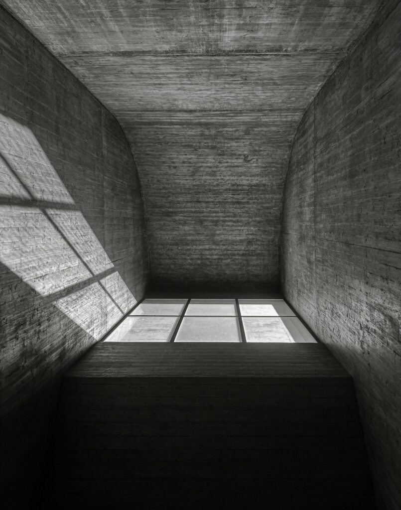 Lucernario sobre un espacio alto de hormigón encofrado, con la luz dibujando la ventana sobre el muro