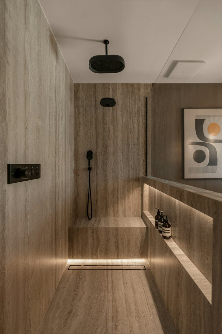 Ducha revestida de travertino veteado con luz rasante